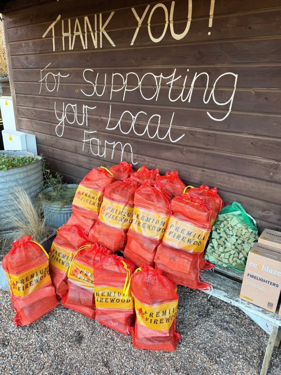 Bags of firewood under the hand-painted &ldquo;Thank you for supporting your local farm&rdquo; sign